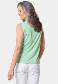 Mintgroene mouwloze top met een relaxte pasvorm, gemaakt van zacht materiaal, gecombineerd met witte broeken. Gladde textuur en eenvoudig ontwerp.