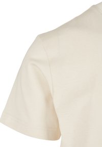 Licht beige T-shirt met korte mouwen, gemaakt van zachte katoen. Heeft een ronde hals en een net gestikte zoom, met een gladde, gelijkmatige textuur.
