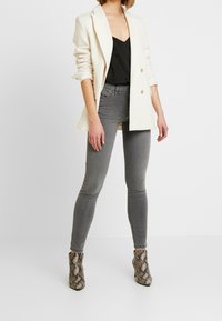 Blazer blanco entallado sobre un top negro de escote en V, combinado con vaqueros pitillo grises y botines de estampado de serpiente. Tejidos suaves y diseño ajustado.