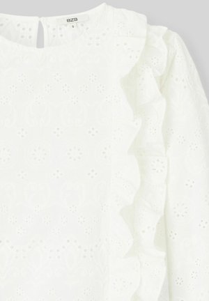 Blouse blanche avec motif floral en œillet, coutures latérales froncées et fermeture en goutte d'eau à l'arrière. Texture douce et tissu léger.