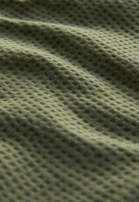 Olivově zelená texturovaná látka s mřížkovým vzorem, vyrobená z měkkého a mírně pružného materiálu. Povrch vypadá zmačkaně a plynule.