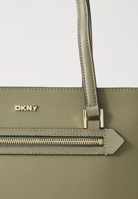 Borsa DKNY verde oliva in materiale testurizzato con tracolla rimovibile, dotata di hardware dorato e una tasca con zip.