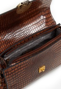 Braune Handtasche mit Krokodil-Prägung und strukturierten Oberflächen, ausgestattet mit einem goldenenverschluss und zwei Innenfächern mit Reißverschluss.