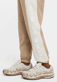 Béžové a biele tenisky Nike P-6000 kombinované s béžovými teplákmi Nike s bielym pruhom a logom na nohe.