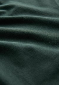 Zbliżenie na ciemnozielony materiał z miękkimi fałdami i widoczną, drobną strukturą tkaniny.
