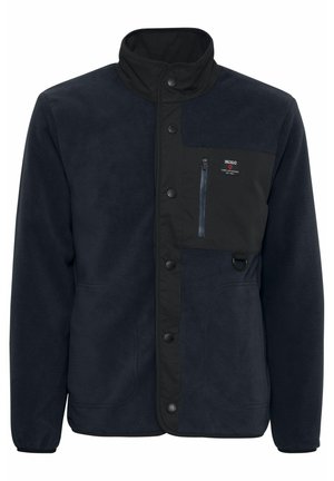 Marinblå fleecejacka med dragkedjeförsedd bröstficka, knappstängning och hög krage. Slät textur med kontrasterande svarta detaljer.
