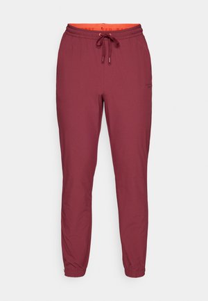 Calças de jogging bordeaux com cintura elástica e cordão, punhos ajustados e uma marca discreta na perna esquerda. Textura de tecido suave.