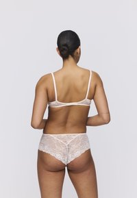 Koronkowy zestaw bielizny w delikatnym odcieniu różu, z subtelnym kwiatowym wzorem. Biustonosz ma cienkie, regulowane ramiączka, a pasujące majtki mają wycięty fason.