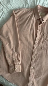 Svetlo roza kord kavbojska srajca z dolgimi rokavi, ovratnikom na gumbe, žepom na sprednji strani in belimi gumbi. Ima rebrasto teksturo in ravno spodnjo rob.