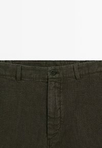 Dark green linen pants featuring a button closure, belt loops, and a textured fabric. The waistband is neatly finished with subtle stitching.