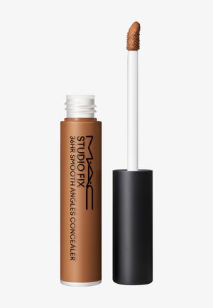 Tube ouverte de correcteur liquide couleur beige moyen avec une baguette blanche et un applicateur incliné, étiqueté MAC Studio Fix 36HR Smooth Angles Concealer.