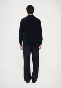 Musta korkean nuhri kauluspaidassa, napitettu hihansuu ja suora leikkaus, yhdistettynä pystysuoriin tummiin housuihin. Sileä rakenne, rento istuvuus.