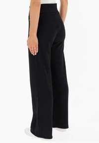 Pantaloni neri a gamba larga in tessuto rigato con vita alta, caratterizzati da un tessuto testurizzato e una vestibilità rilassata. Cuciture sottili lungo i lati.