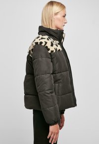 Pufferjack met een donker groene body en een beige luipaardprint kraag. Voorzien van een ritssluiting en elastische manchetten. Heeft een gladde textuur en een gewatteerd ontwerp.