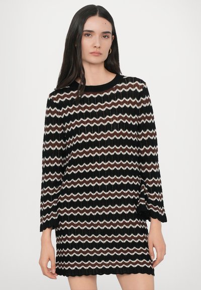 Robe tricotée en zigzag noire, marron et crème avec des manches longues, un col rond et un ourlet en feston. Tissu texturé et léger avec trame ouverte.