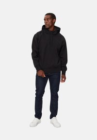 Sudadera negra con capucha y bolsillo tipo canguro, puños y dobladillo acanalados, combinada con jeans de mezclilla oscura y zapatillas blancas.