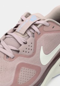 Κοντινό πλάνο ενός ροζ αθλητικού παπουτσιού Nike με λευκό λογότυπο "swoosh", πάνελ από δίχτυ και ροζ κορδόνια περασμένα από τις τρύπες.