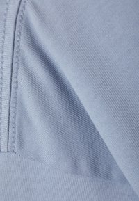 Světle modrá tkanina s jemnou strukturou a jemným tkaním. Podél okraje je šev, který zdůrazňuje pružnost materiálu.