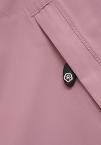 Ljust rosa tyg med en slät textur, med en svart knapp med en logo, en sydd söm och en sned fickdesign.