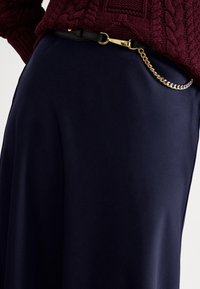 Tengerészkék szatén szoknya sima textúrával, fekete övvel, amely arany csattal és összekapcsolt arany lánc díszítéssel rendelkezik.