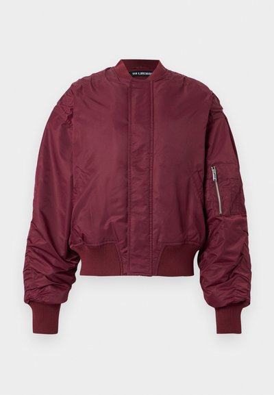 Blouson aviateur bordeaux avec une poche zippée sur le bras, des poignets côtelés et une texture lisse et brillante. Présente un col montant et une coupe courte.