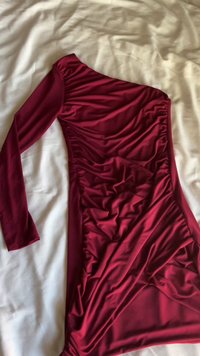 Vestido de uma ombro, com manga comprida, na cor vermelho profundo. Feito de um tecido suave, apresenta detalhes franzidos ao longo do lado e uma textura drapeada em toda a peça.