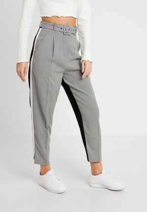 Pantalon à taille haute à carreaux avec des bandes noires et blanches sur les côtés, une ceinture assortie, associé à des baskets blanches et un top court blanc à manches longues.