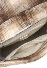 Interiér béžové a hnědé chlupaté kabelky s kovovou kapsou na zip a krémovým látkovým oddílem.