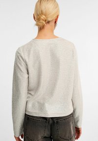 Sølvfarvet tekstureret langærmet top med rund halsudskæring og en let cropped længde. Har en glitrende finish og subtile linjer.