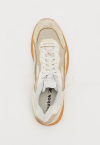 Adidași bej, realizați din plasă și suede, cu un limba albă, talpă din cauciuc portocalie și un logo vizibil pe lateral.