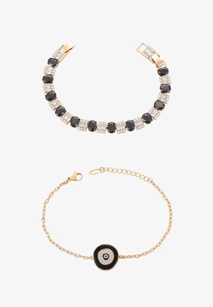 Złote bransoletki z czarnymi i przejrzystymi kamieniami szlachetnymi; jedna ma naprzemienny wzór owalny i kwadratowy, druga posiada okrągły czarno-biały amulet w kształcie oka.