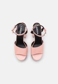 Paire de sandales à talon bloc ouvertes rose avec brides à la cheville et semelles intérieures noires, vue de dessus sur un fond blanc uni.