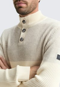 Gehaakt pullover in lichtcrème met een geribbelde textuur, voorzien van een hoge kraag en drie donkere knopen aan de voorkant.