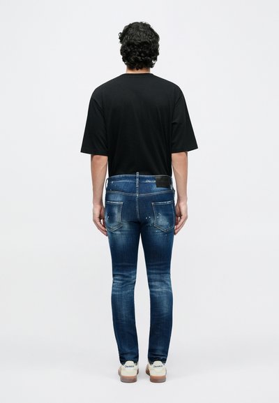 Μαύρο υπερμεγέθες T-shirt, μπλε εφαρμοστά τζιν με ξεθώριασμα και φθορές, μαύρο δερμάτινο ταμπελάκι στη μέση, λευκά αθλητικά με σόλες από καουτσούκ.