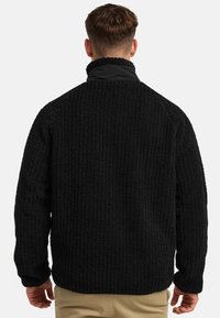 Black fleece pullover with a textured, ribbed surface. High collar and long sleeves; relaxed fit. Soft, warm material ideal for layering.