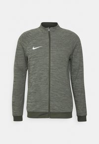 Chaqueta con cremallera Nike en verde oscuro, hecha de tejido texturizado, presenta un cuello alto y un logo blanco en el lado izquierdo del pecho.