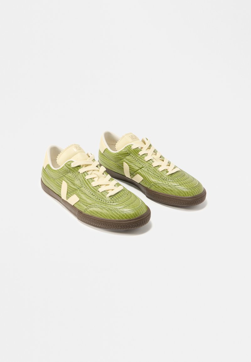 Paire de baskets basses vert clair avec lacets crème, languette talonnière beige et semelles marron foncé sur fond blanc.