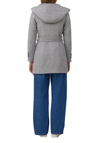 Manteau en laine gris avec capuche, taille ceinturée et design ajusté. En dessous, un pantalon en denim bleu à larges jambes et des poignets côtelés aux chevilles.