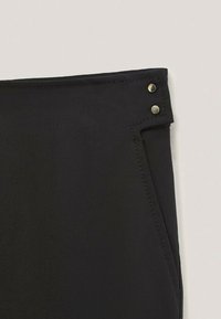 Zwarte stoffen broek met een gladde textuur, voorzien van zilveren hardware accentueringen bij de taille en een gestructureerd ontwerp.