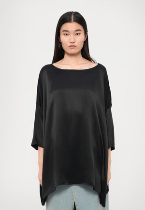 Zwarte oversized top met een bootnek en driekwart mouwen, gemaakt van zachte, gladde stof met een subtiele textuur en een gedrapeerde vorm.