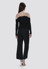 Schwarzes, geripptes Langarmoberteil mit kühlen Schulter-Ausschnitten und dünnen Trägern, kombiniert mit lockeren schwarzen Hosen und silbernen High-Heels.