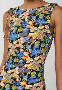 Mouwloos topje met bloemenpatroon in het zwart, voorzien van kleurrijke bloemen in blauw, oranje en groen, met verstelbare strikdetails op de schouders.