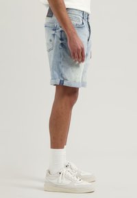 Helle blaue Jeansshorts mit umgeschlagenem Saum, Fünf-Taschen-Design und leichtem Used-Look. Kombiniert mit weißen Socken und Sneakers.