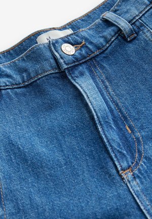 Jeans i denim med en blekt mellanblå färg, med knäppning och kontraststickning. Tyget har en slät yta.