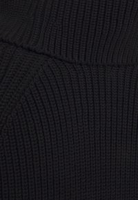 Zwart ribbelstof met een gestructureerde afwerking, voorzien van verticale lijnen en een licht verhoogd patroon. Zacht gebreid materiaal, van gemiddelde dikte.