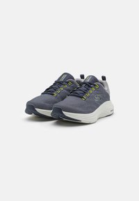 Scarpe sportive con tomaia in rete blu navy e accenti gialli, suola bianca imbottita e suola in gomma testurizzata per una migliore trazione.