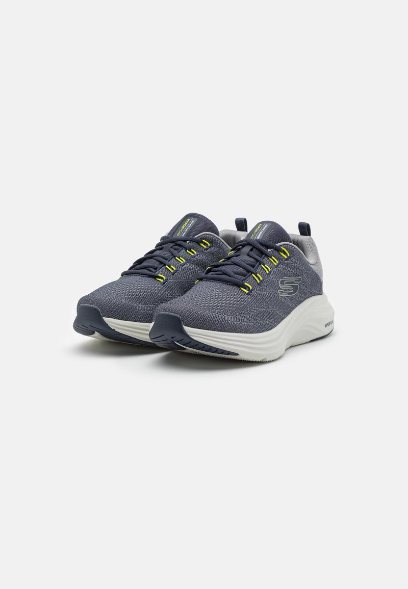 Buty sportowe z granatowej siateczki z żółtymi akcentami, białą amortyzującą podeszwą oraz teksturowaną gumową podeszwą dla lepszej przyczepności.