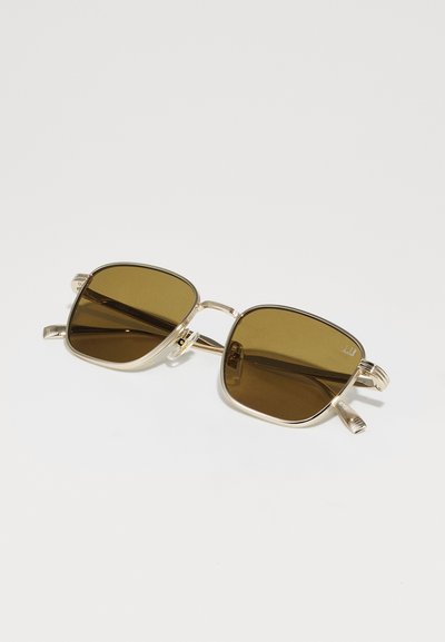 Lunettes de soleil en métal avec une monture dorée et des verres carrés marron. Les branches présentent un design texturé et des accents décoratifs sur les charnières.