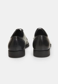 Scarpe nere in pelle con una finitura liscia, punta arrotondata e una suola piatta in gomma bassa. Presentano un design minimalista e senza hardware visibile.