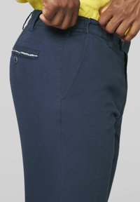 Marineblaue Hosen mit glatter Textur, ausgestattet mit einer Gesäßtasche mit einem dekorativen Muster und einem Knopfverschluss.